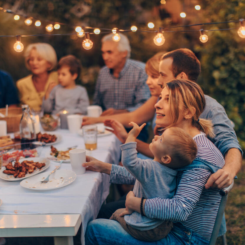 Family gathered around an outdoor dining table with string lights overhead